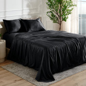 Black satin bedding set on a bed in a bedroom with a plant and window in the background.
