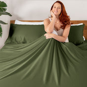 Woman sitting on a bed with TENCEL bedding and pillowcases.