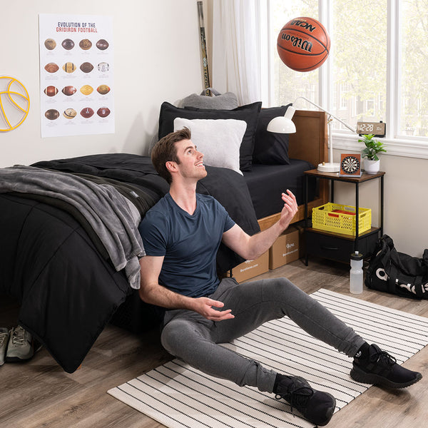 Young Guy leaning again dorm bed playing with a basketball
