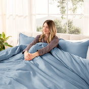 Woman lying on a bed with organic sateen bedding in a bright room with large windows.