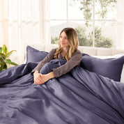 Woman lying on a bed with organic sateen bedding in a bright room with large windows.