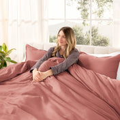 Woman lying on a bed with organic sateen bedding in a bright room with large windows.