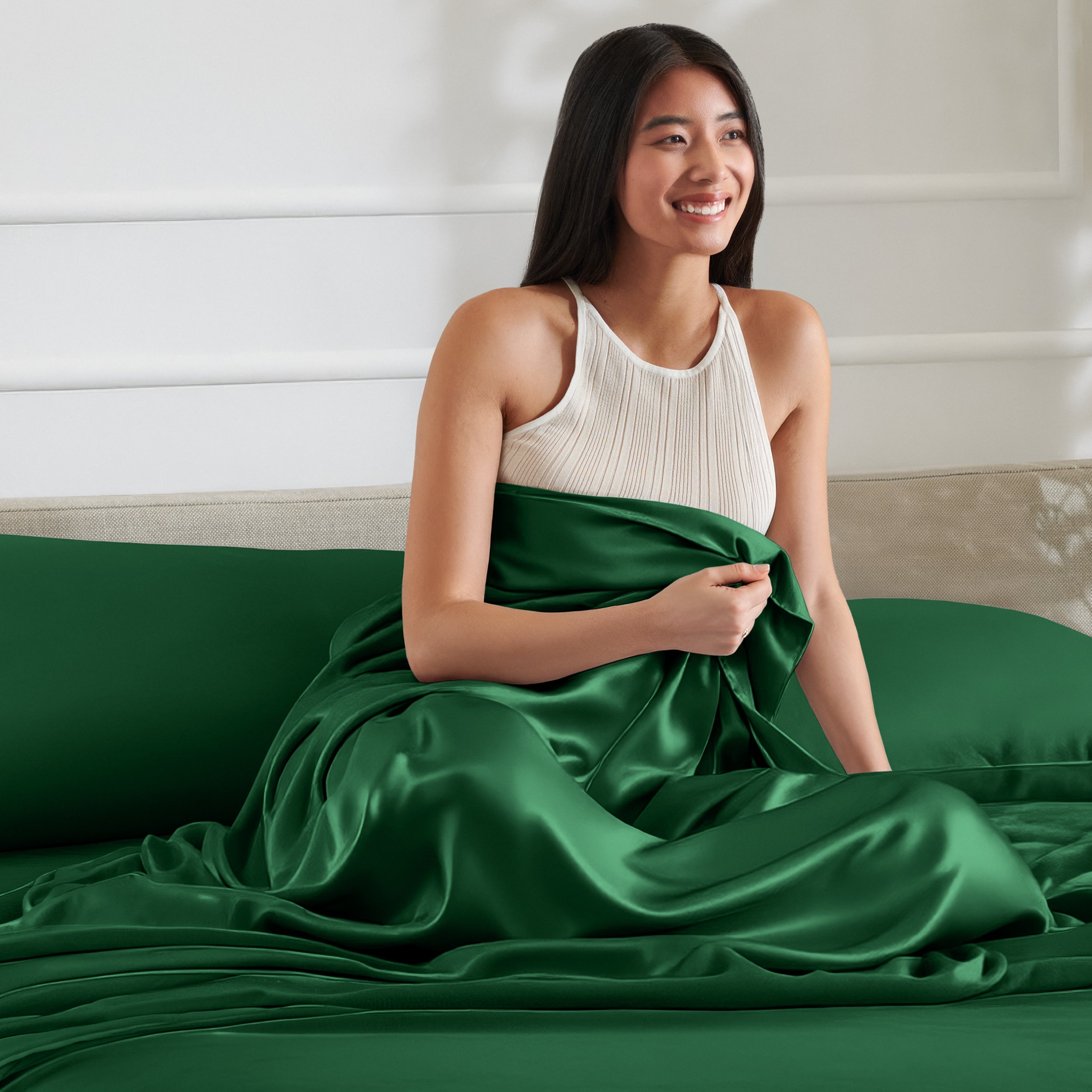 Woman sitting on a bed with a satin sheet over her