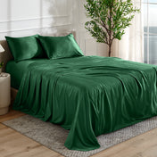 Forest green satin bedding set on a bed in a bedroom with a plant and window in the background.
