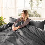 Woman lying on a bed with organic sateen bedding in a bright room with large windows.