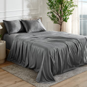 Grey satin bedding set on a bed in a bedroom with a plant and window in the background.