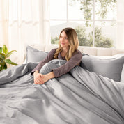 Woman lying on a bed with organic sateen bedding in a bright room with large windows.