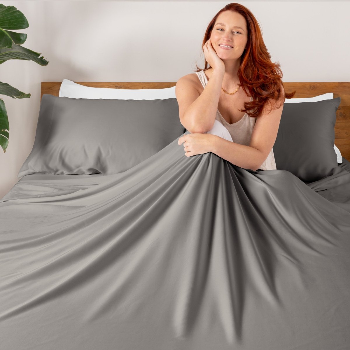 Woman sitting on a bed with TENCEL bedding and pillowcases.