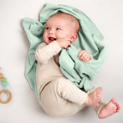 A baby lying on a receiving blanket. She has her thumb in her mouth.