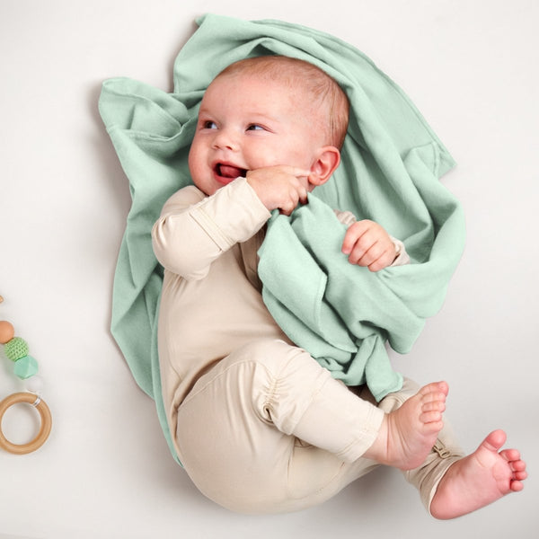 A baby lying on a receiving blanket. She has her thumb in her mouth.