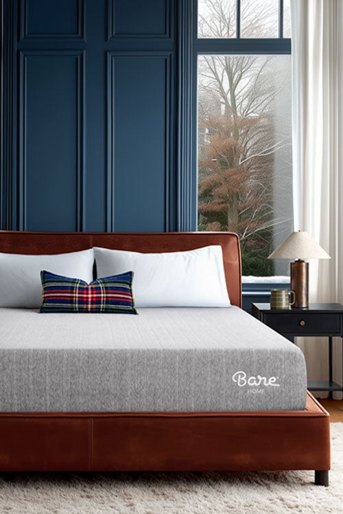 Bedroom with a bed featuring a plaid pillow and 'Bare' mattress brand visible, against a blue paneled wall with large windows.