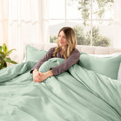 Woman lying on a bed with organic sateen bedding in a bright room with large windows.