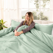 Woman lying on a bed with organic sateen bedding in a bright room with large windows.