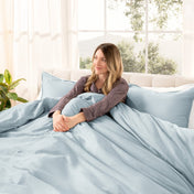 Woman lying on a bed with organic sateen bedding in a bright room with large windows.