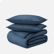 A folded organic sateen duvet cover with two pillows on top.