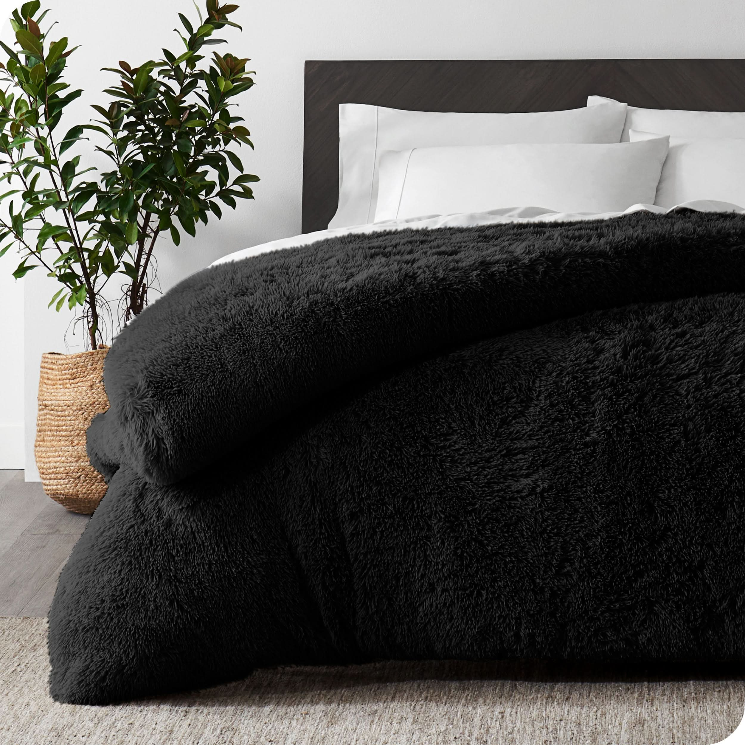 A black shaggy duvet cover on a bed with white sheets and pillowcases. A large plant is next to the bed.