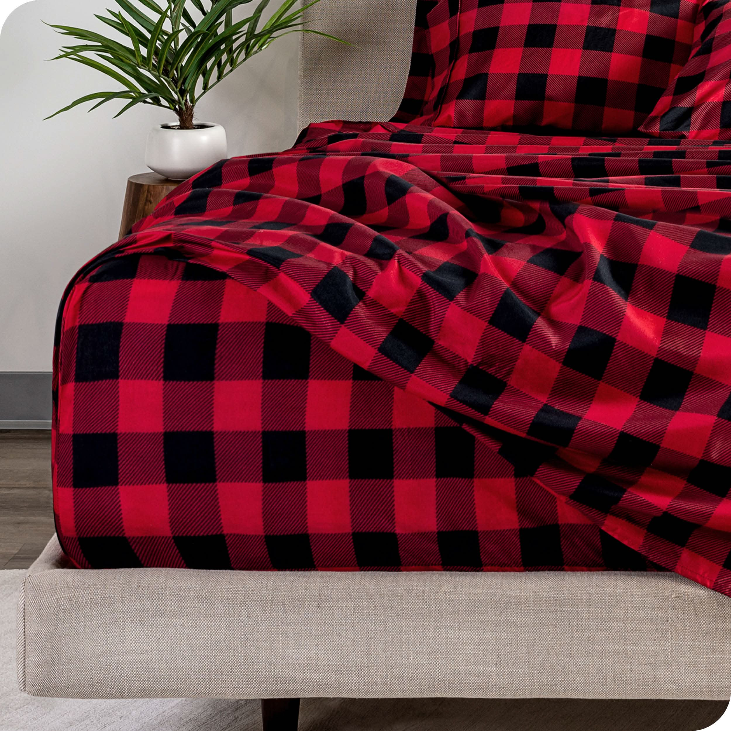 Close up of the end of a mattress and bed frame with plaid sheets on the bed.