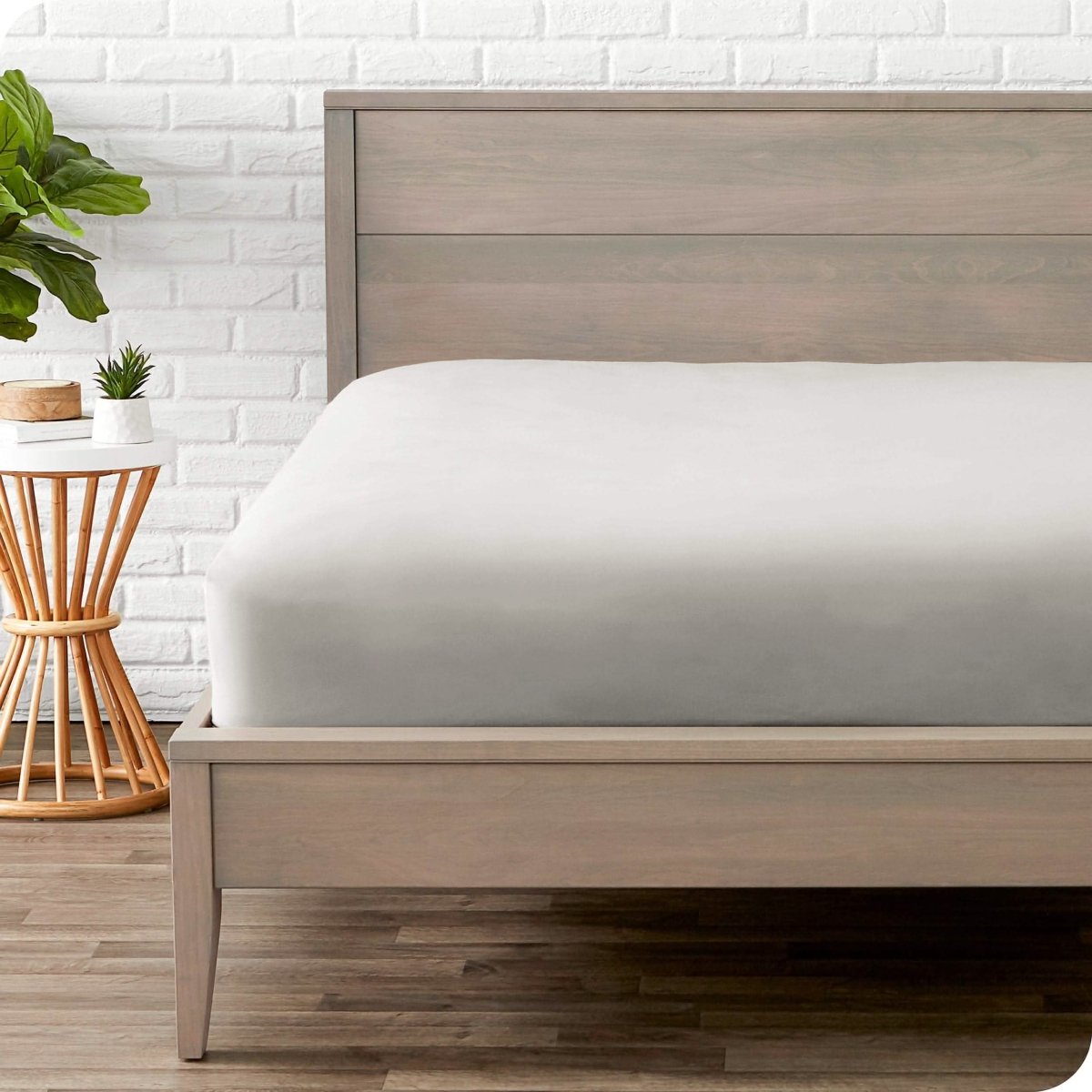 Bedroom with a microfiber fitted sheet on the mattress. A small nightstand is next to the bed with a plant and a bowl on it.