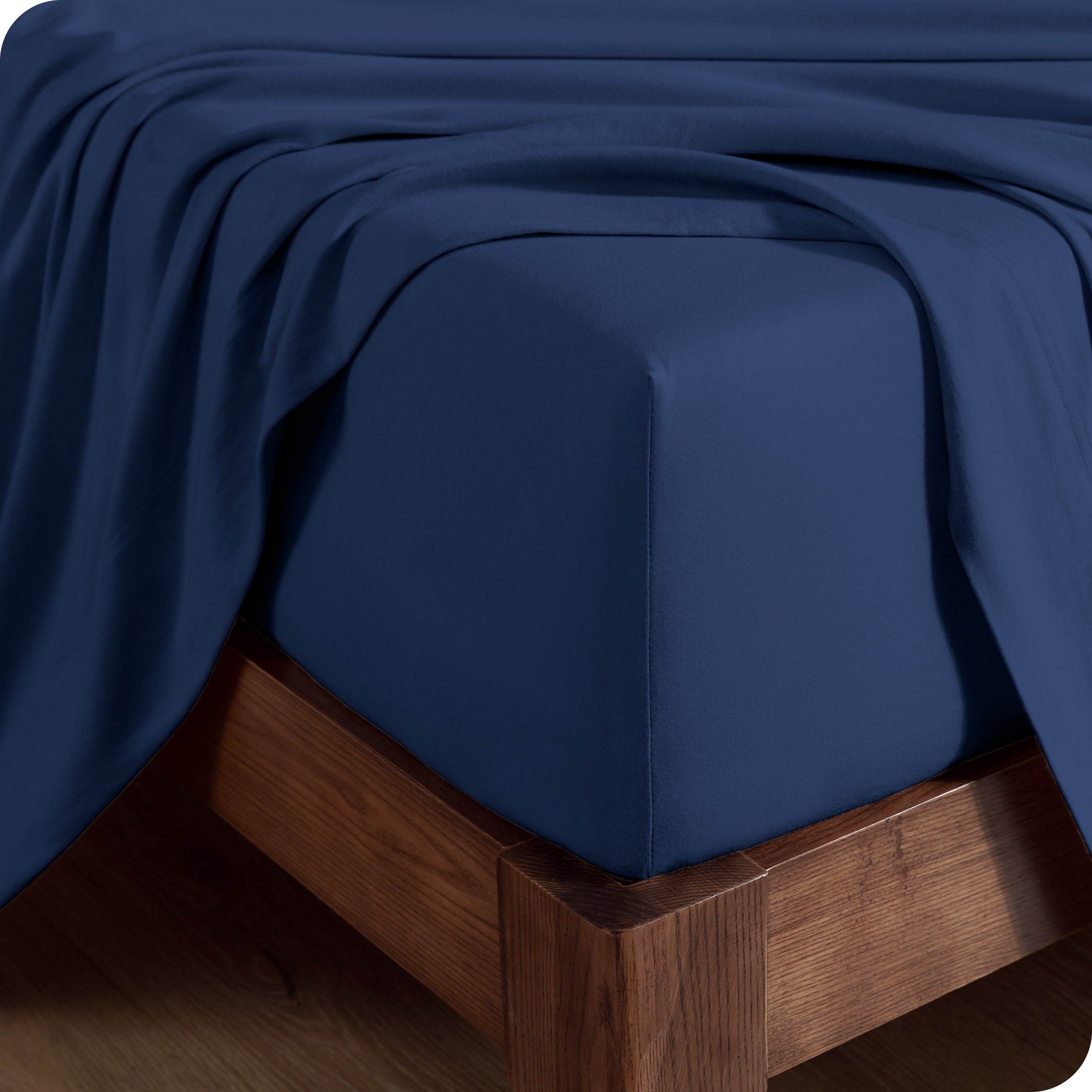 Close up of the corner of a mattress with a fitted sheet on it and a top sheet hanging over the side