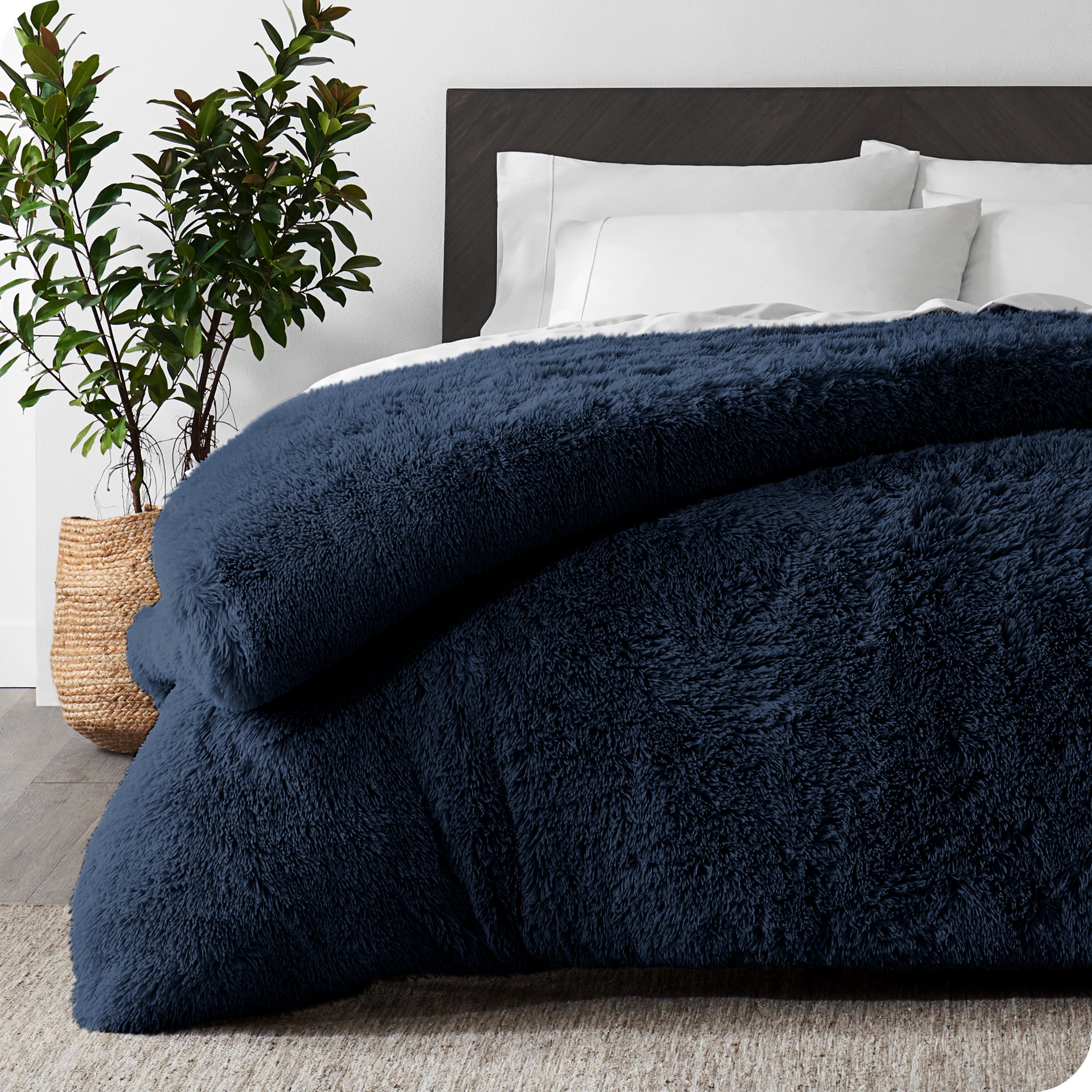 A dark blue shaggy duvet cover on a bed with white sheets and pillowcases. A large plant is next to the bed.