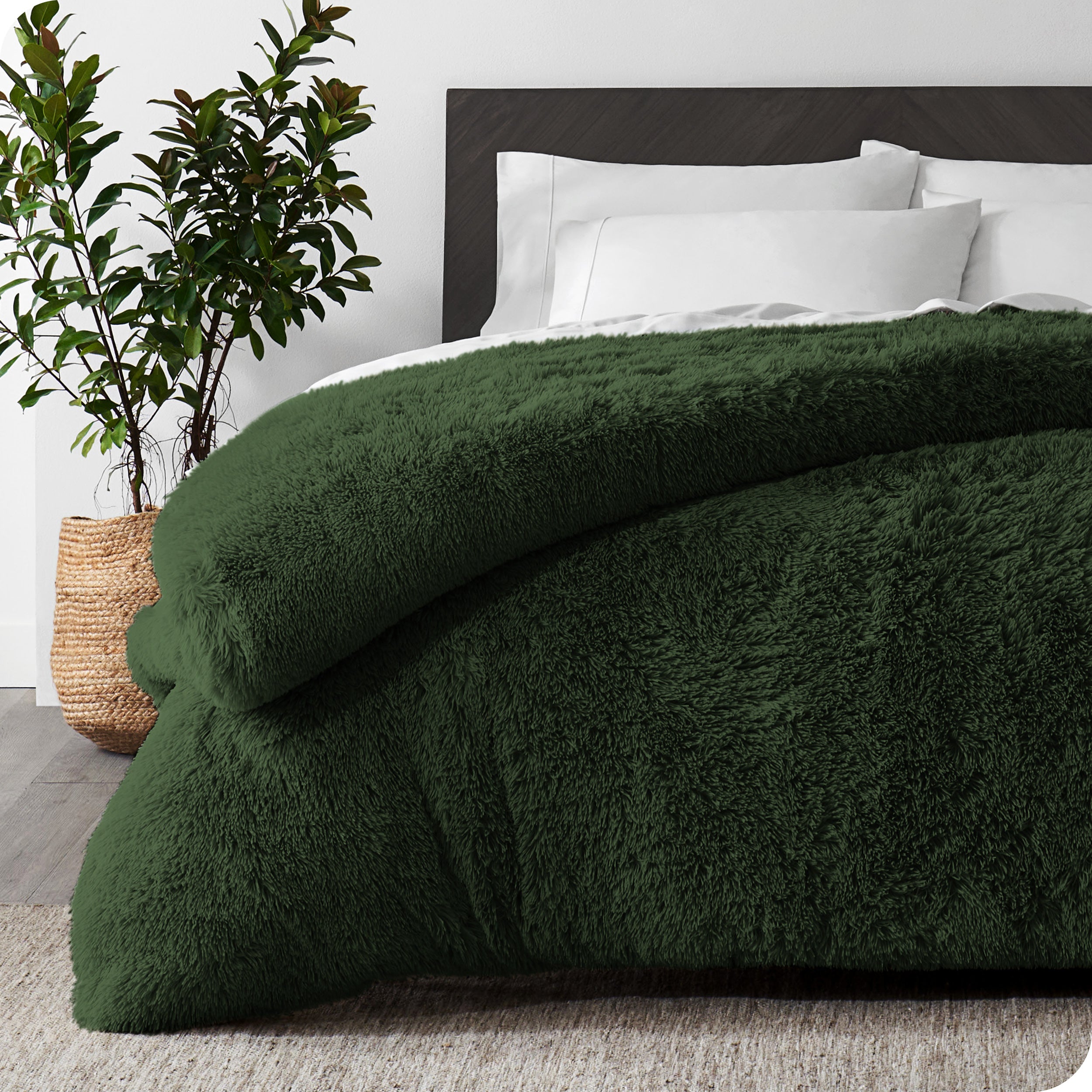 A forest green shaggy duvet cover on a bed with white sheets and pillowcases. A large plant is next to the bed.