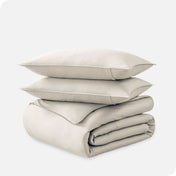 A folded organic sateen duvet cover with two pillows on top.