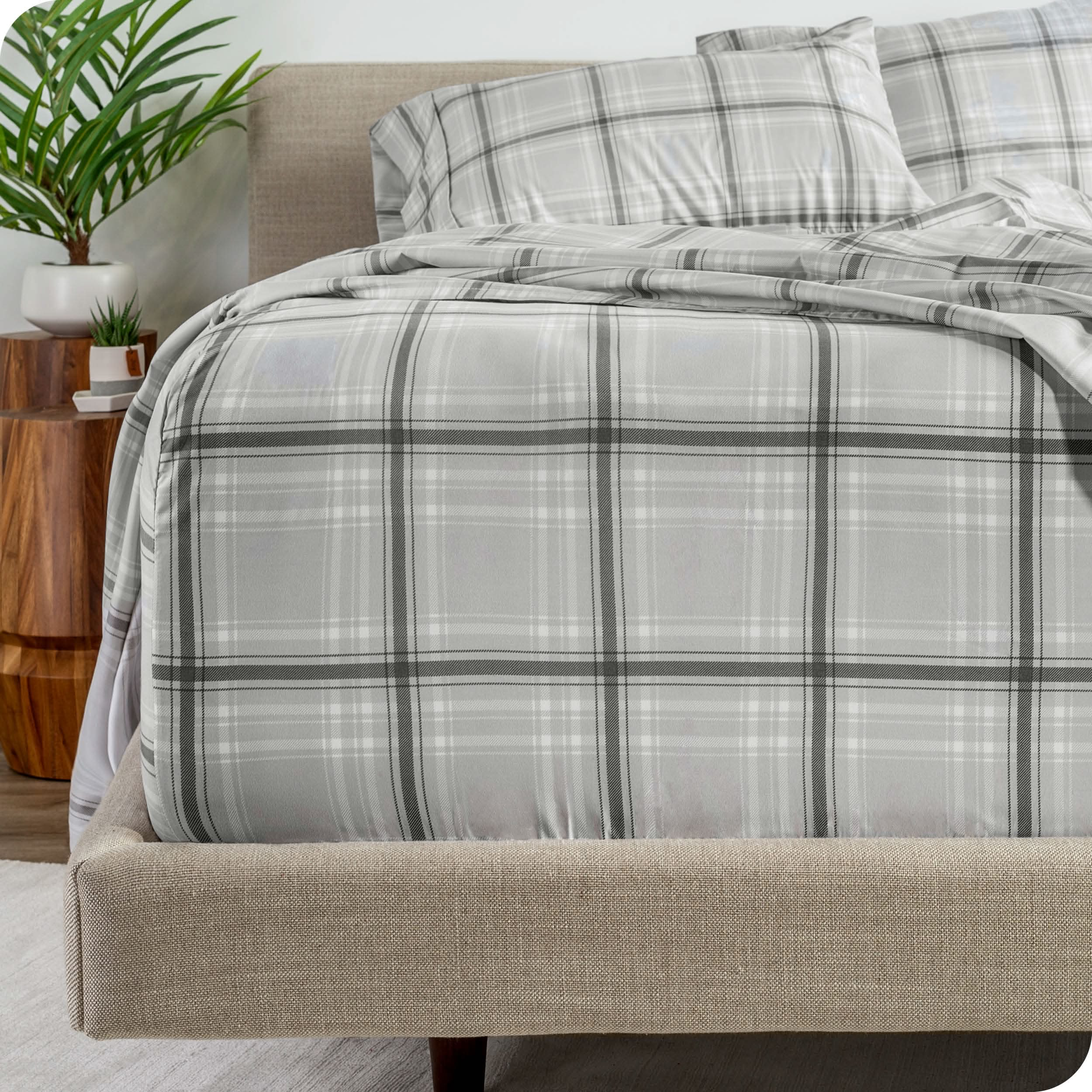 Close up of the end of a mattress and bed frame with plaid sheets on the bed.