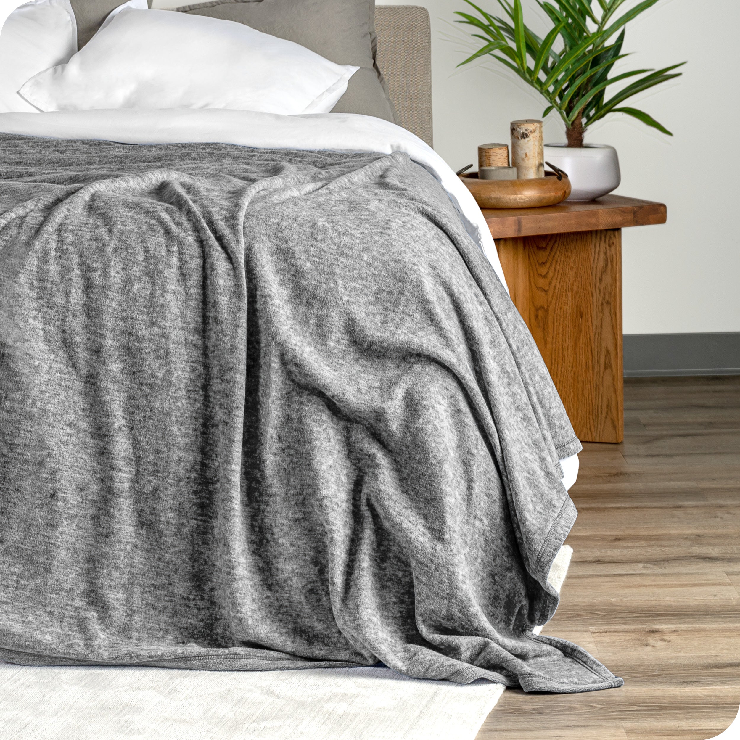 A polar fleece blanket drapped over the side and the end of a bed made with all white bedding
