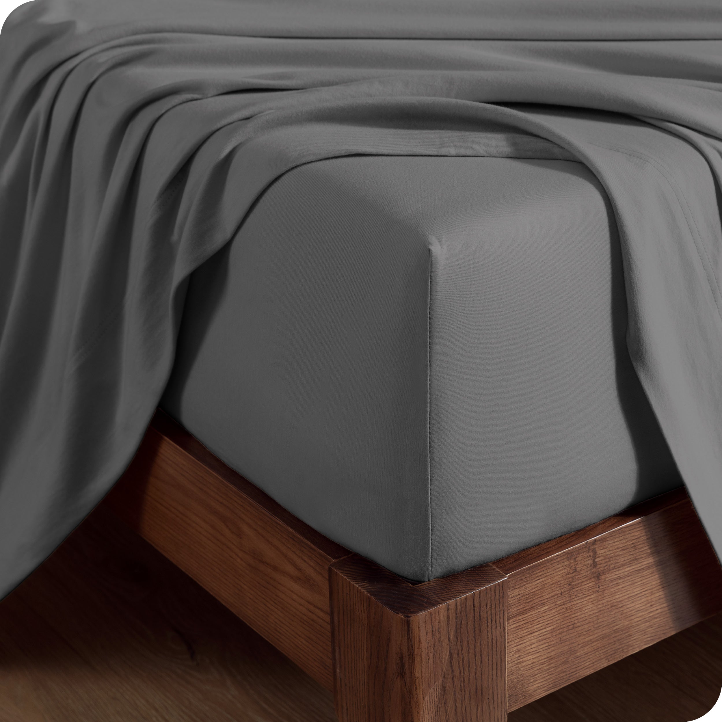 Close up of the corner of a mattress with a fitted sheet on it and a top sheet hanging over the side