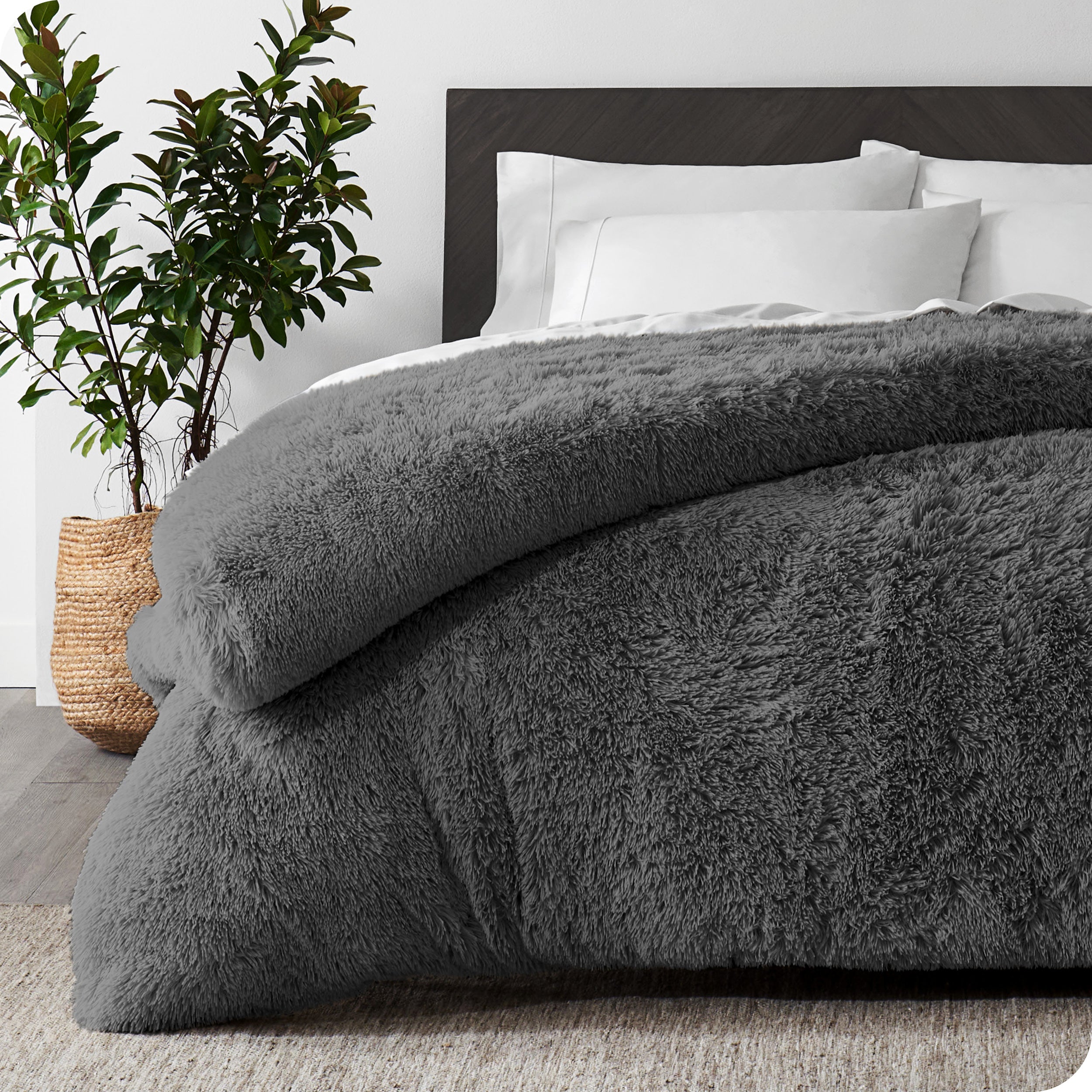 A grey shaggy duvet cover on a bed with white sheets and pillowcases. A large plant is next to the bed.