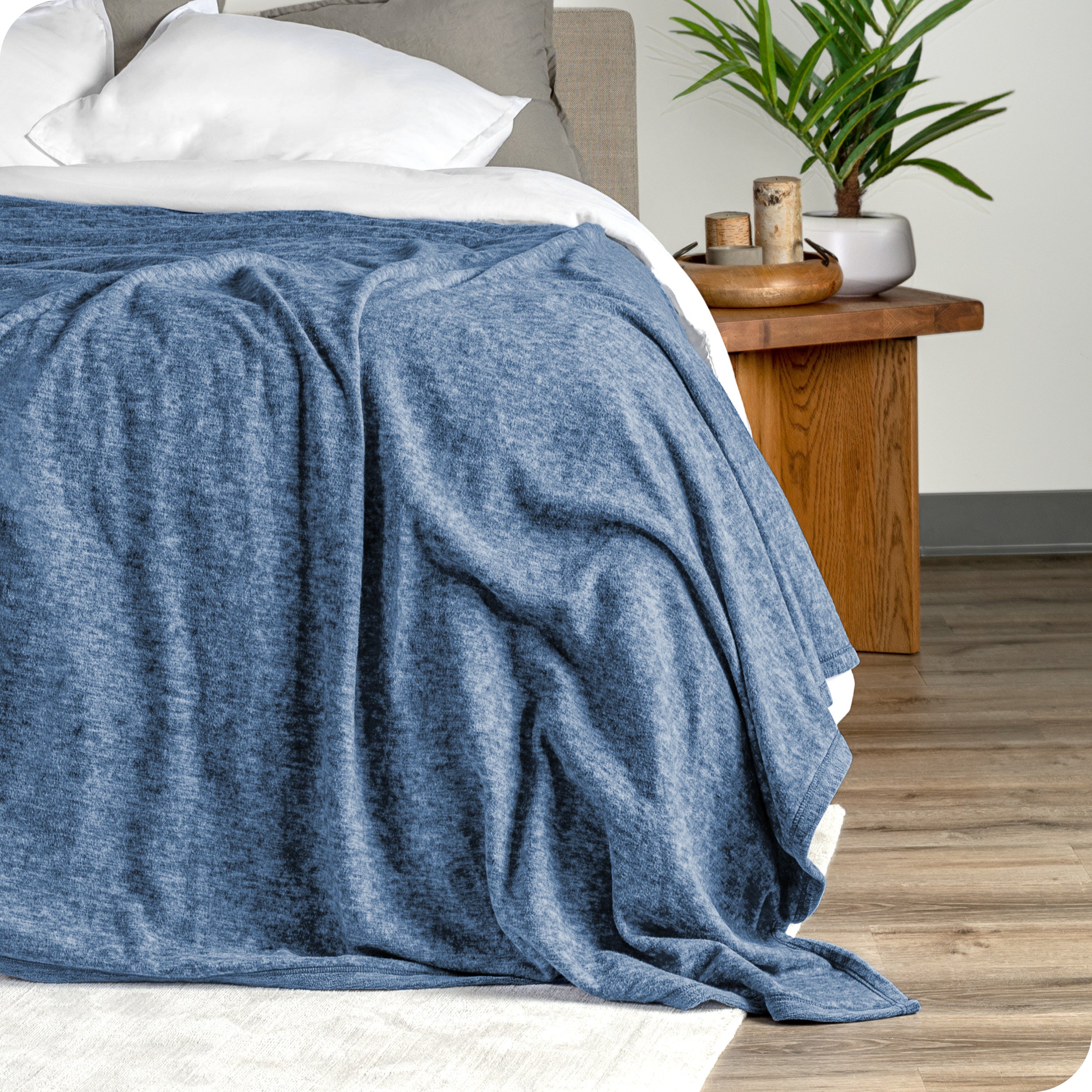 A polar fleece blanket drapped over the side and the end of a bed made with all white bedding