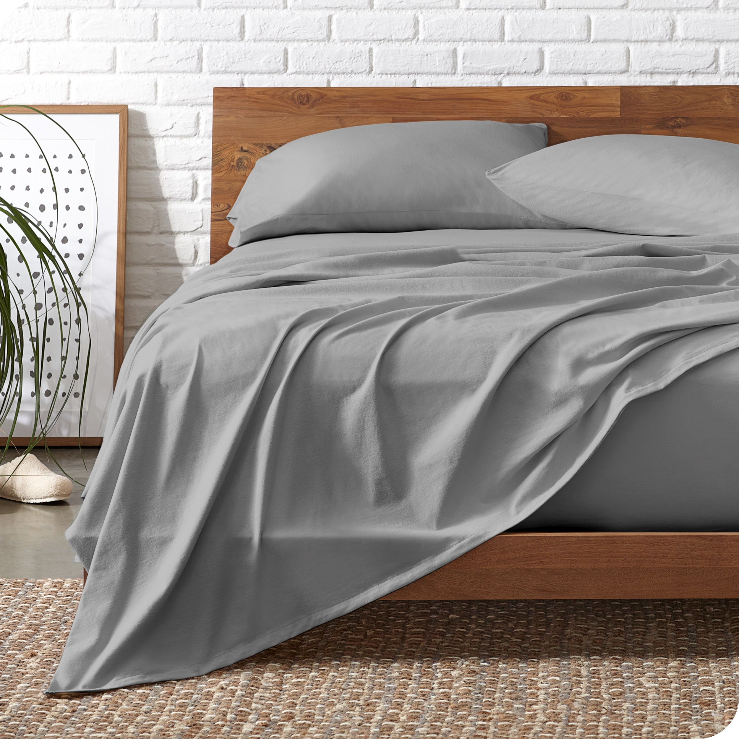 Wooden bed frame with light grey organic cotton jersey sheets on the bed