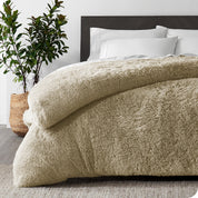 A sand shaggy duvet cover on a bed with white sheets and pillowcases. A large plant is next to the bed.