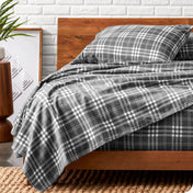 Wooden bed frame with flannel print sheets on the bed