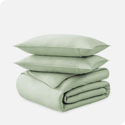 A folded organic sateen duvet cover with two pillows on top.