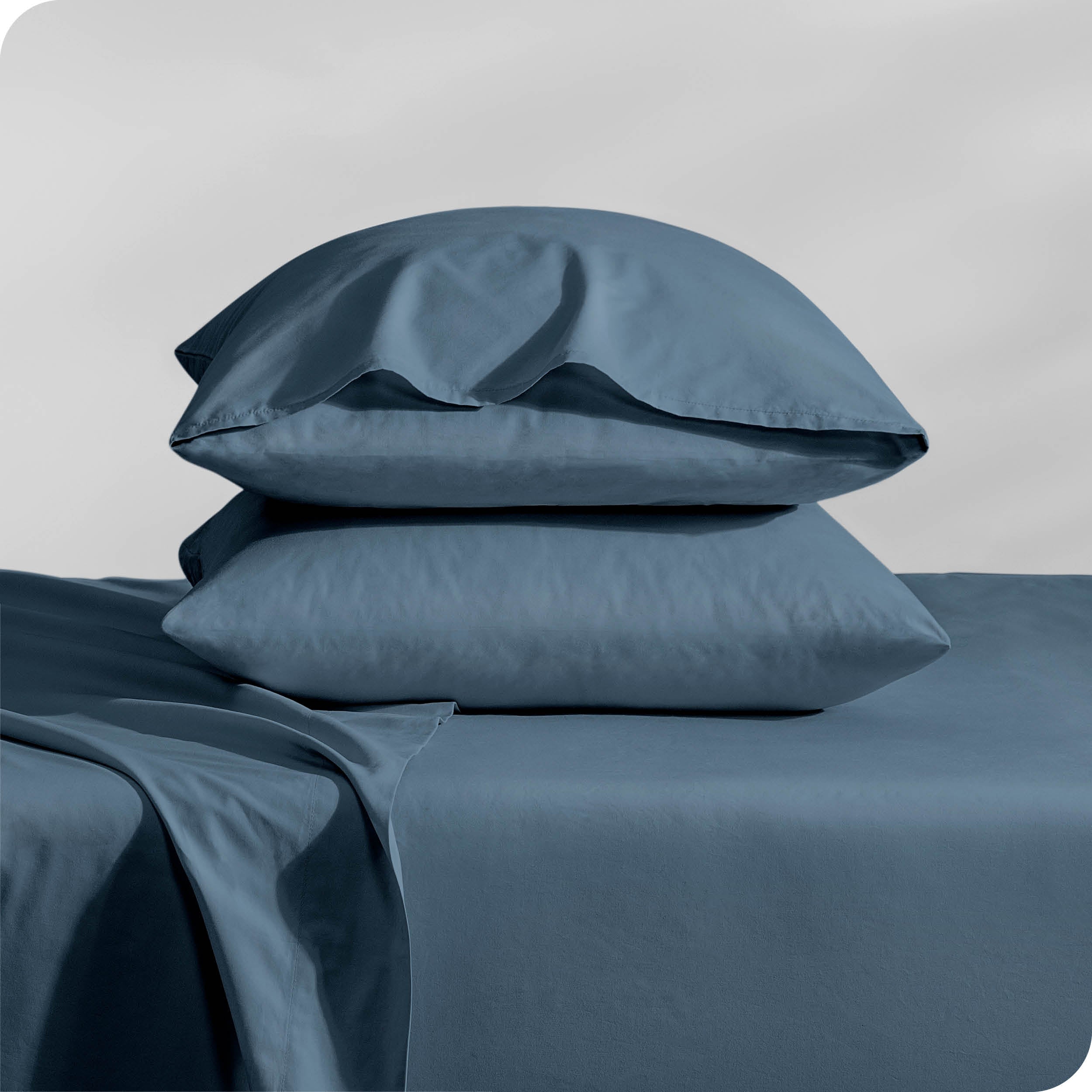 Pillows inside percale pillowcases stacked on a bed