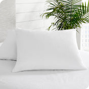 Two pillows covered with protectors sitting on a mattress covered in a mattress protector. A tall plant is next to the bed.