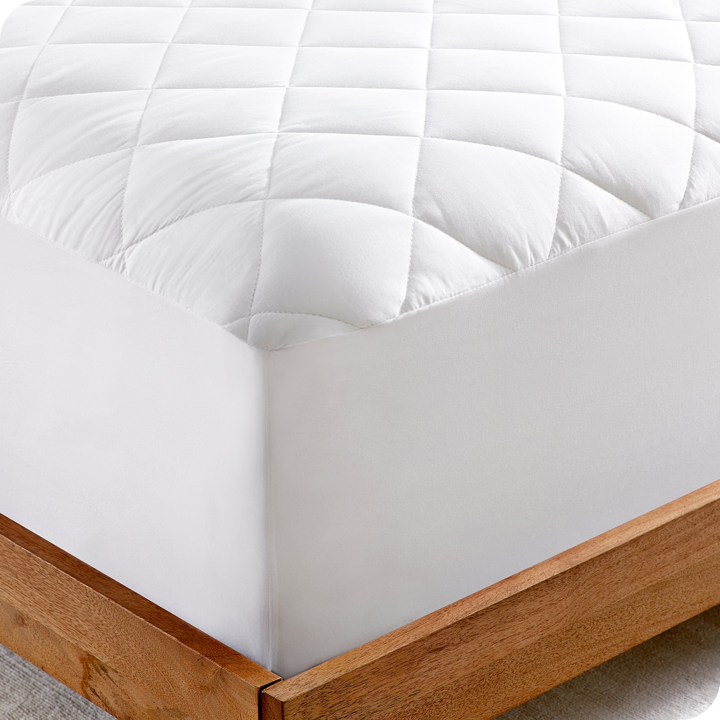 Corner of a mattress on a wood bed frame. A white quilted mattress pad is covering the mattress.